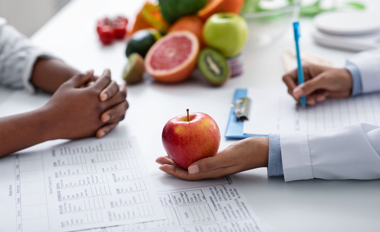 Diététicienne Aubagne. Plan de nutrition avec des fruits sur la table ainsi qu'un bloc note utilisée par une diététicienne, patient en face de la diététicienne